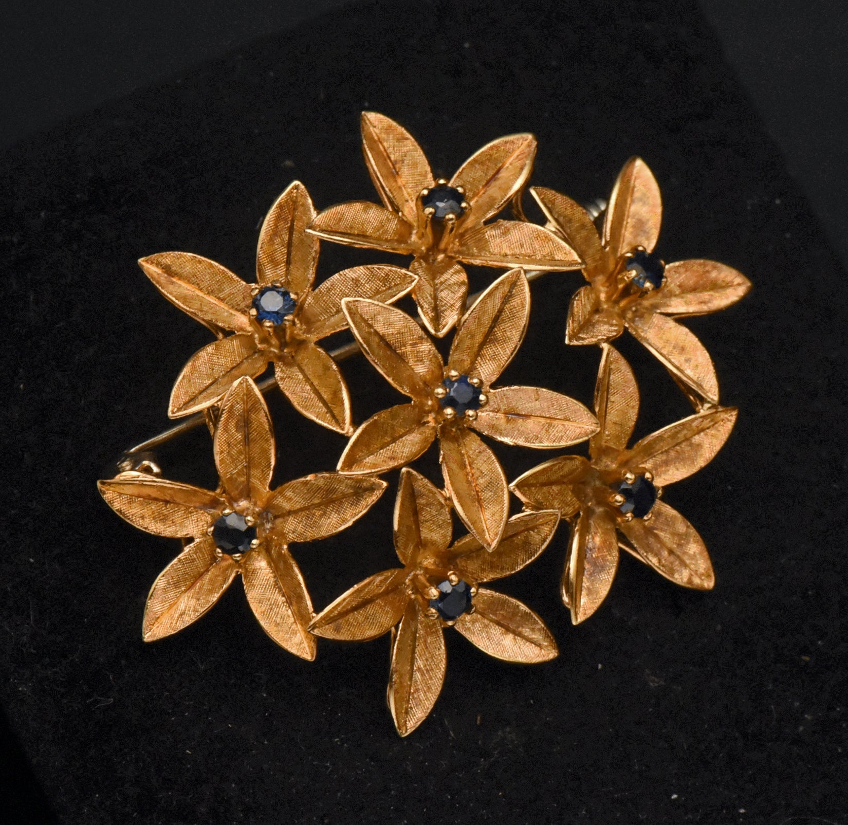 Stunning vintage antique handcrafted 18k gold brooch consisting of seven flowers with florentine finish, each set with a round cut sapphire.