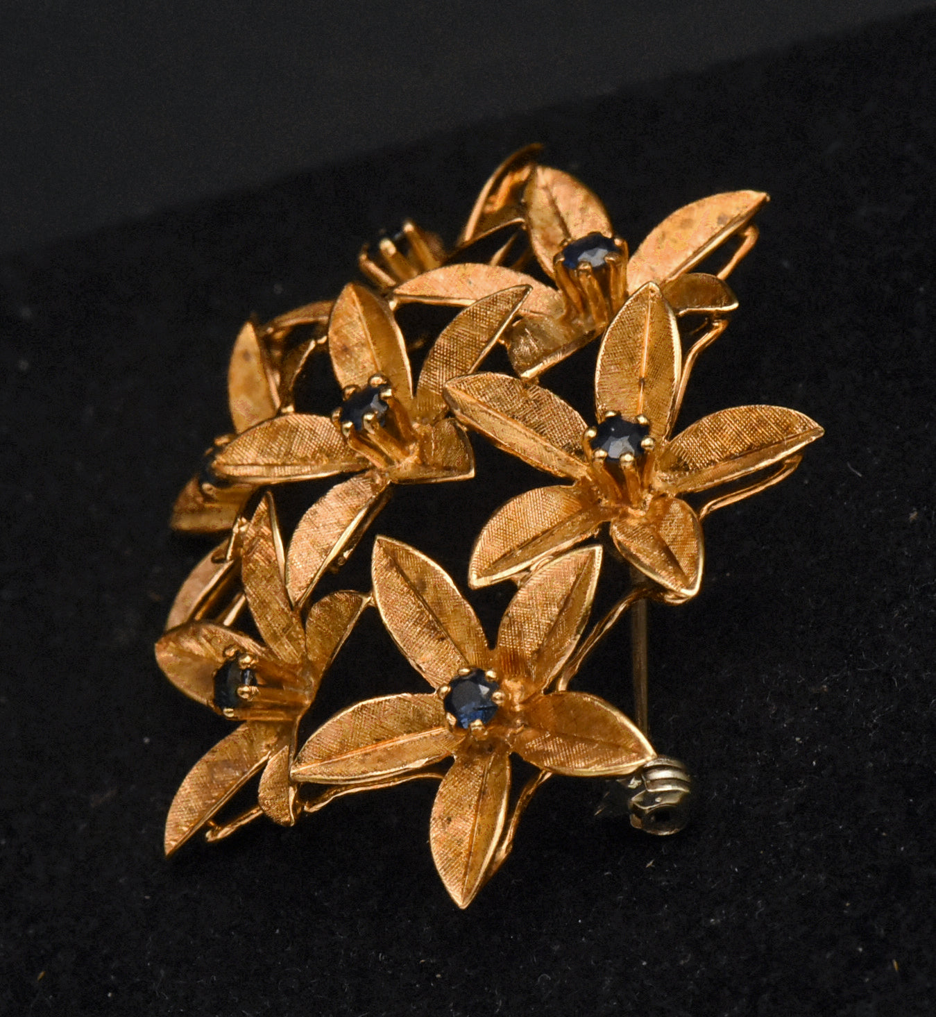 Stunning vintage antique handcrafted 18k gold brooch consisting of seven flowers with florentine finish, each set with a round cut sapphire.