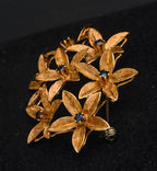 Stunning vintage antique handcrafted 18k gold brooch consisting of seven flowers with florentine finish, each set with a round cut sapphire.