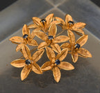 Stunning vintage antique handcrafted 18k gold brooch consisting of seven flowers with florentine finish, each set with a round cut sapphire.